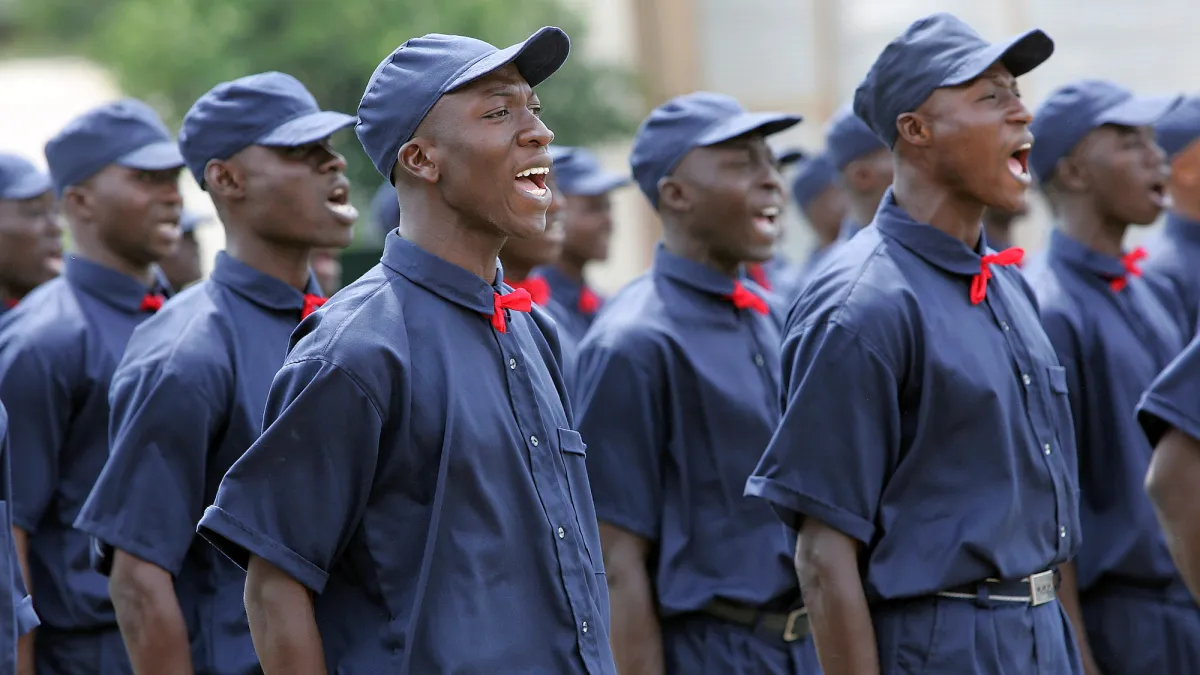 Auxiliary police cadets respond to commands at the inauguration ceremony of their new training centre in Bouake, Côte d'Ivoire. police cadets wearing blue uniforms with red ties standing in formation