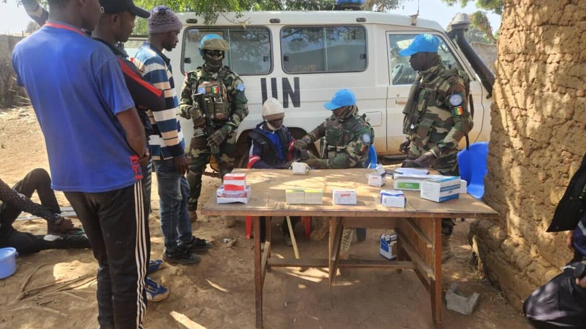 Community members and peacekeepers meet around an outdoor table, in front of a UN van