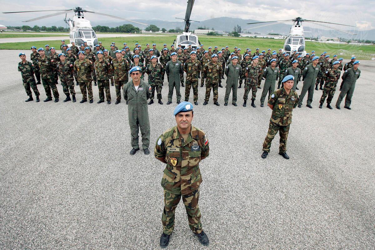 A battalion of Chilean soldiers in uniformed lined up in front of three helicopters. In front of the soldiers is their leader.