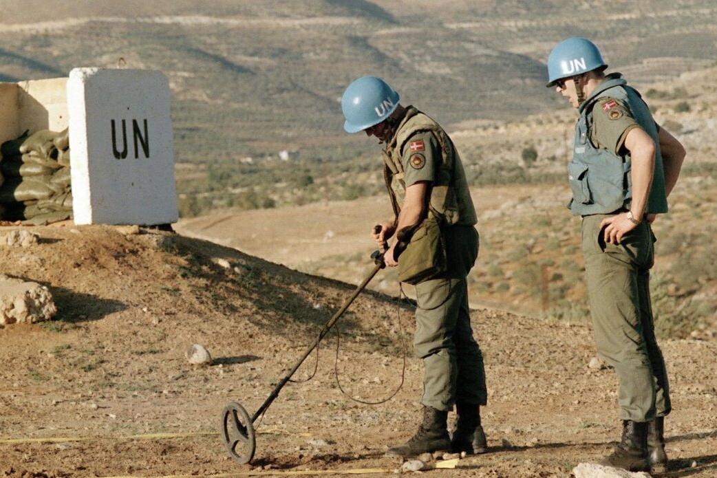 Peacekeepers use metal detection equipment in a vast area.