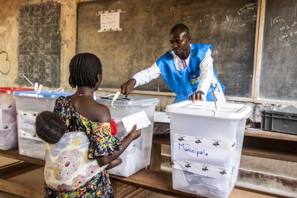Un agent électoral aide un électeur à déposer son bulletin.