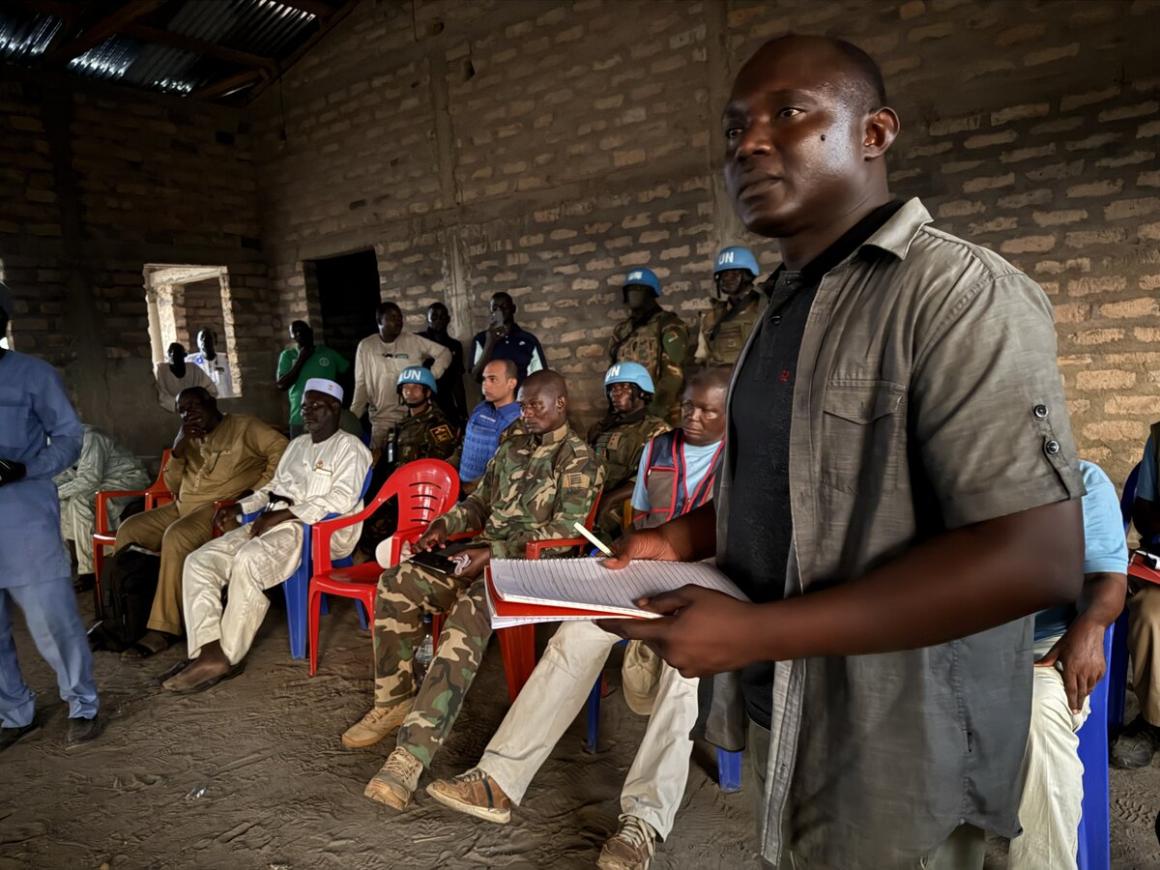 Un homme se tient debout devant un groupe de personnes assises, tenant un bloc-notes.