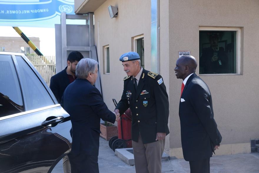 UN Secretary General shakes hands with a uniformed officer near a vehicle outside a building, while another person stands nearby